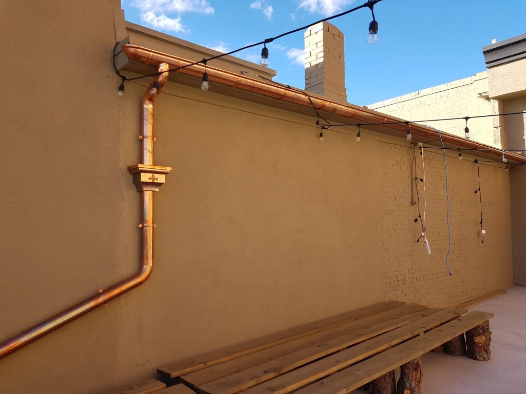 A commercial property with a flat roof and visible copper commercial gutters running along a back wall.